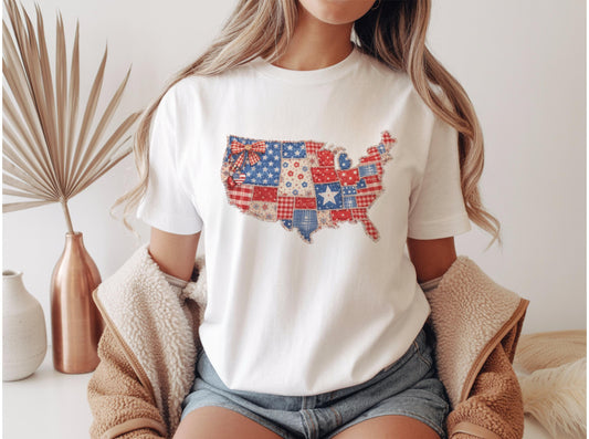May include: White t-shirt featuring a patchwork design of the United States map in red, white, and blue. The design incorporates stars, stripes, and floral patterns. The shirt is a casual wear item.