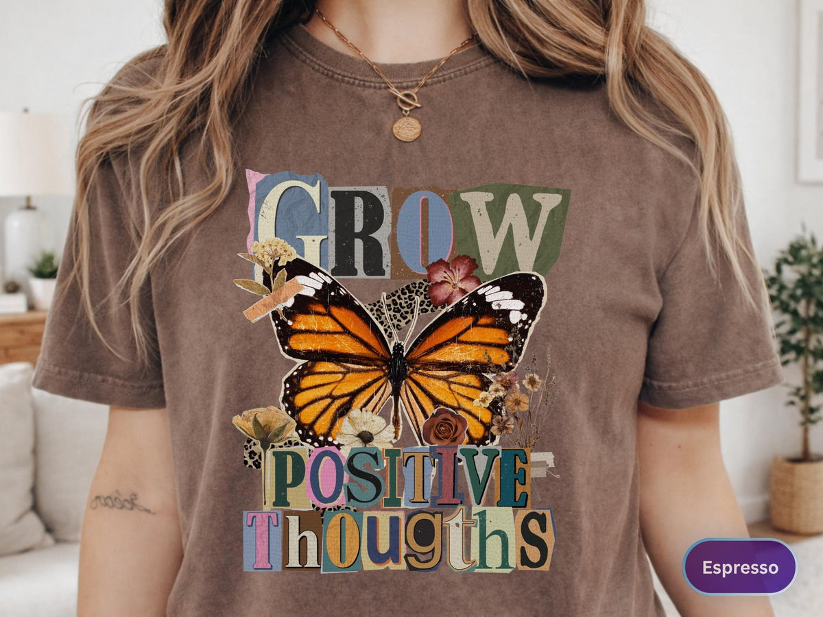 May include: Espresso-colored t-shirt featuring a large butterfly graphic with orange, black, and white wings. The words "GROW POSITIVE THOUGHTS" are printed above and below the butterfly in a collage style.