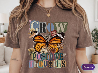 May include: Espresso-colored t-shirt featuring a large butterfly graphic with orange, black, and white wings. The words "GROW POSITIVE THOUGHTS" are printed above and below the butterfly in a collage style.