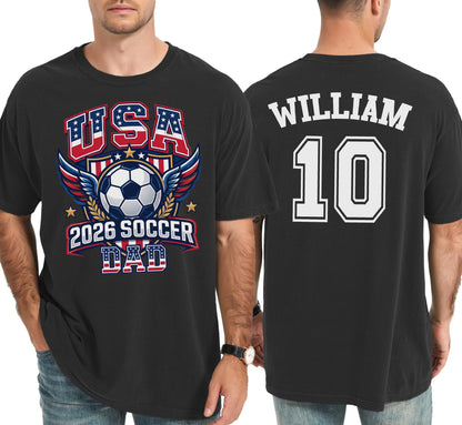 May include: Black t-shirt with "USA 2026 SOCCER DAD" graphic on the front, featuring a soccer ball and wings in red, white, and blue. The back displays "WILLIAM" and the number "10" in white.