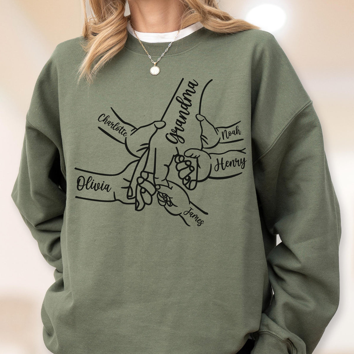 May include: Olive green sweatshirt featuring a graphic of hands holding each other, with the word "Grandma" and the names "Charlotte", "Olivia", "Noah", "Henry", and "James" printed on it. The sweatshirt has a crew neck and long sleeves.