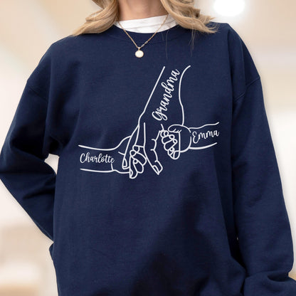 May include: Navy blue sweatshirt featuring a white graphic of three hands holding each other. The word "Grandma" is written on one hand, with "Emma" and "Charlotte" on the other hands. The sweatshirt is a crew neck style.