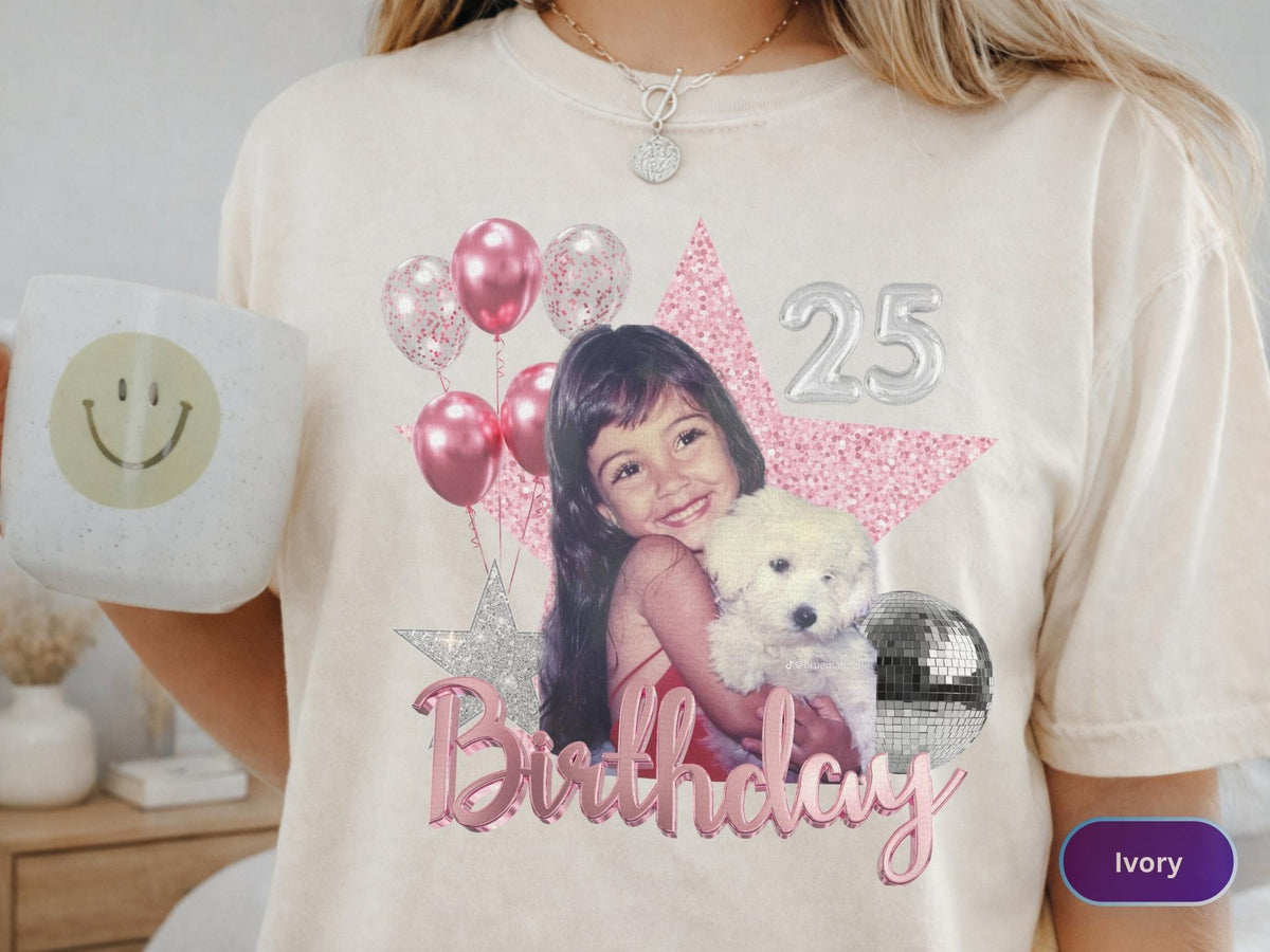 May include: An ivory t-shirt featuring a graphic print of a young child holding a white puppy. The design includes pink balloons, a large pink glitter star, a silver disco ball, the number 25 in silver, and the word Birthday in pink script.