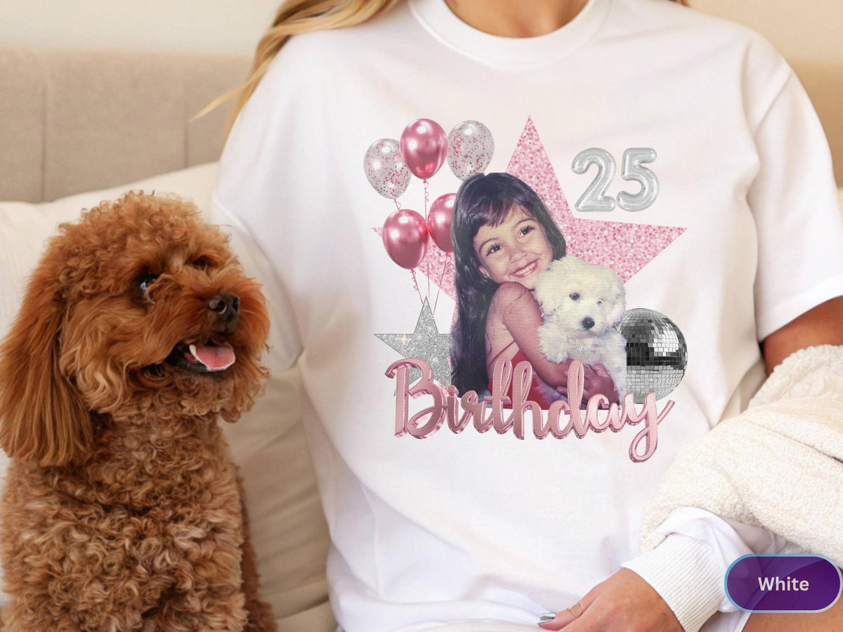 May include: A white t-shirt featuring a graphic print of a young person holding a small white dog. The design includes pink and silver balloons, a large pink star, a silver disco ball, the number 25, and the word Birthday in pink script lettering.
