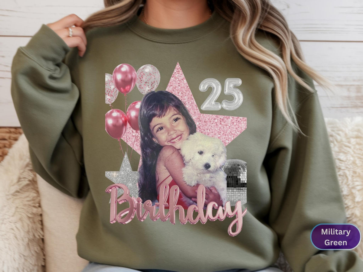 May include: A military green crewneck sweatshirt featuring a graphic print of a young child holding a white puppy. The design includes pink balloons, a large pink glitter star, a silver star, the number 25, and the word Birthday in pink script.