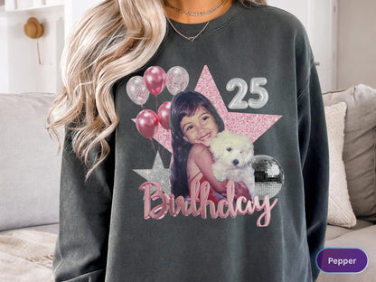 May include: A charcoal gray crewneck sweatshirt featuring a graphic print of a person holding a white puppy. The design includes a large pink glitter star, silver balloons, a disco ball, the number 25, and the word Birthday in pink script lettering.