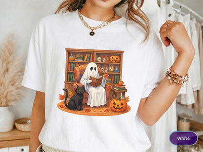 May include: A white t-shirt featuring a graphic print of a ghost sitting in an armchair reading a book, accompanied by a black cat, pumpkins, and a bookshelf filled with books and potions. The design includes autumn leaves on the floor.