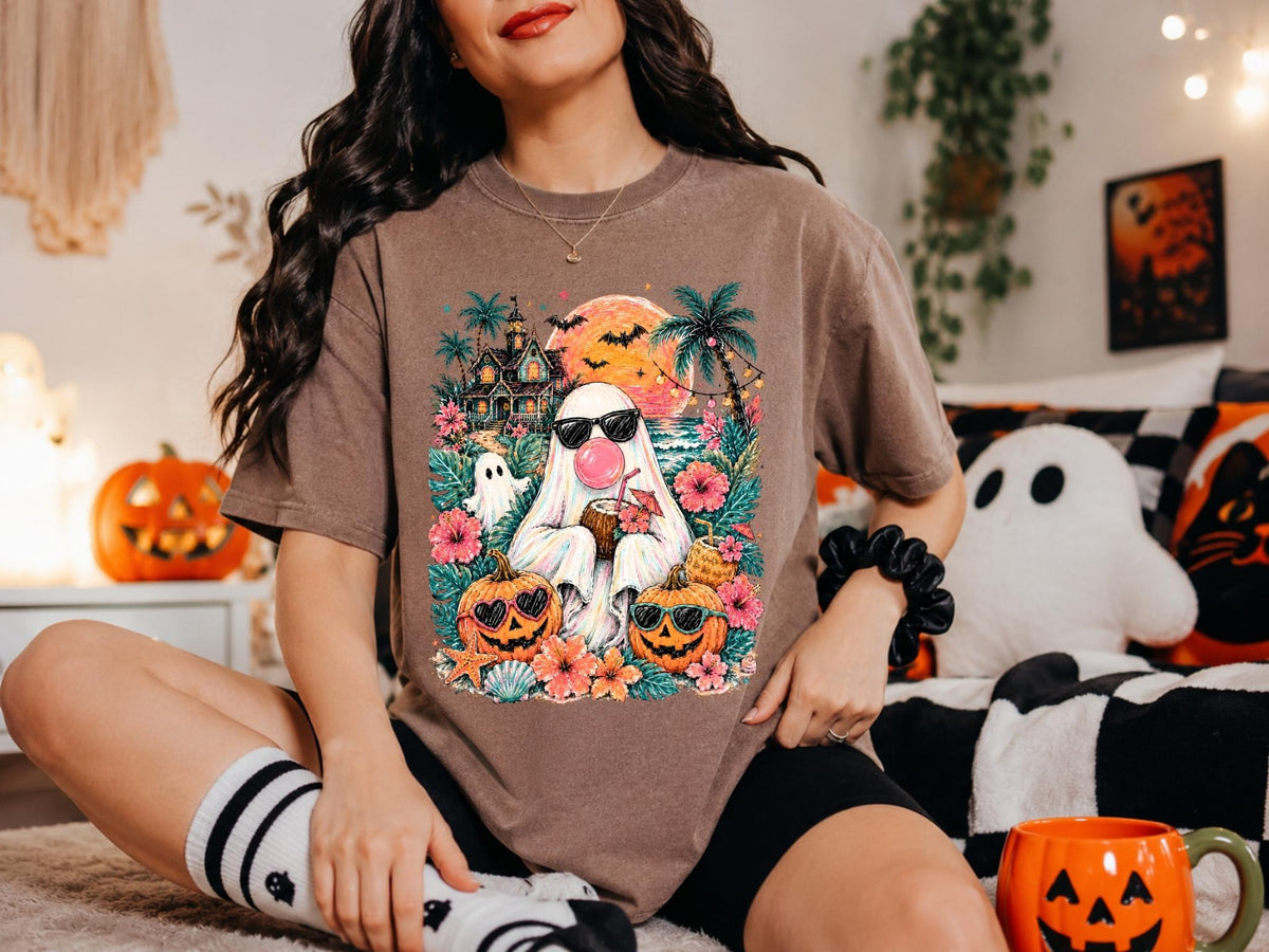 May include: A brown short-sleeve t-shirt featuring a graphic print of a ghost wearing sunglasses and blowing a pink bubble, surrounded by tropical flowers, palm trees, a haunted house, bats, a large orange moon, and two jack-o'-lanterns.