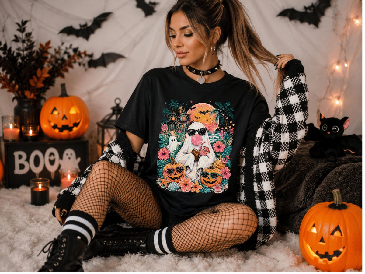 May include: A black short-sleeve t-shirt featuring a colorful graphic print of a ghost wearing sunglasses and blowing a pink bubble, surrounded by tropical flowers, palm trees, a haunted house, a full moon, and two jack-o'-lanterns with sunglasses.