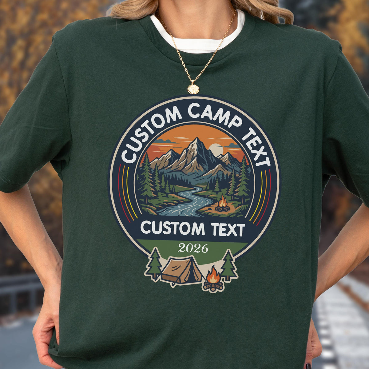May include: A dark green short-sleeve t-shirt featuring a circular graphic with a mountain landscape, a river, and a campfire. The text reads CUSTOM CAMP TEXT at the top, CUSTOM TEXT in the middle, and 2026 at the bottom, with a tent and trees.