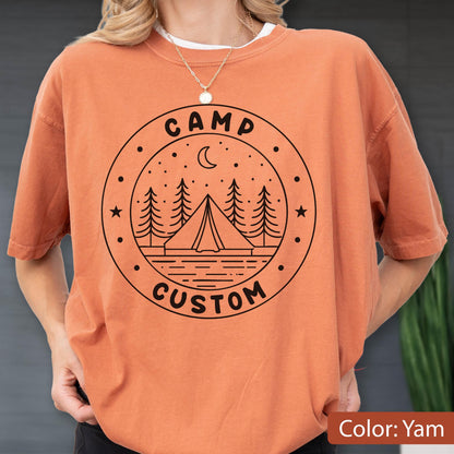 May include: A yam-colored short-sleeve t-shirt featuring a black circular graphic on the chest. The design includes a tent, pine trees, a crescent moon, and stars, with the text CAMP CUSTOM printed in a bold, sans-serif font within the circle.