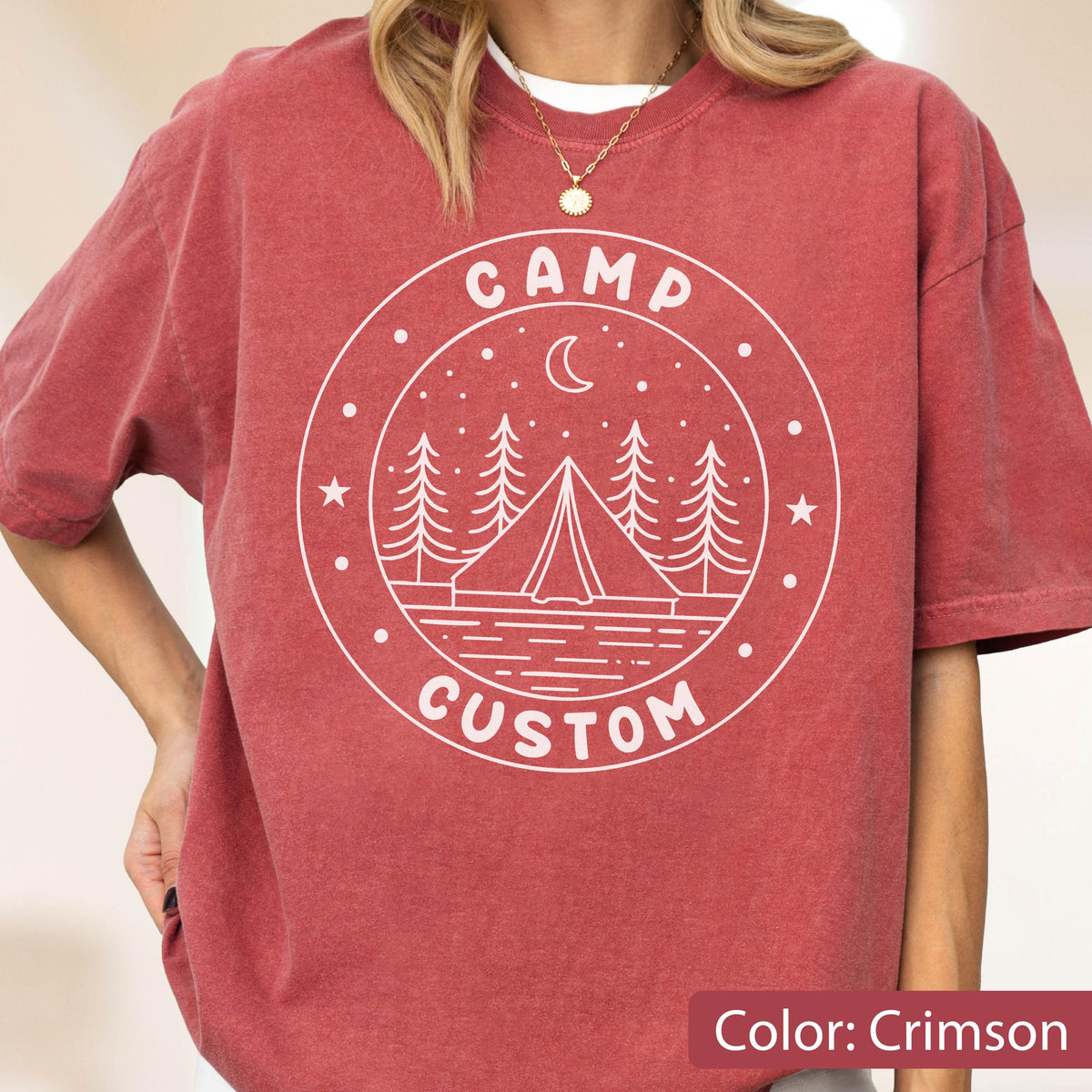 May include: A crimson short-sleeve t-shirt featuring a white circular graphic on the chest. The design includes a tent, pine trees, a crescent moon, and stars, with the text CAMP CUSTOM printed in a circular layout around the central illustration.