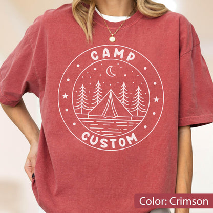 May include: A crimson short-sleeve t-shirt featuring a white circular graphic on the chest. The design includes a tent, pine trees, a crescent moon, and stars, with the text CAMP CUSTOM printed in a circular layout around the central illustration.