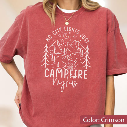May include: A crimson short-sleeve t-shirt featuring a white graphic print of mountains, pine trees, a crescent moon, stars, and a campfire. The text reads NO CITY LIGHTS JUST CAMPFIRE Nights in a mix of block and script lettering.