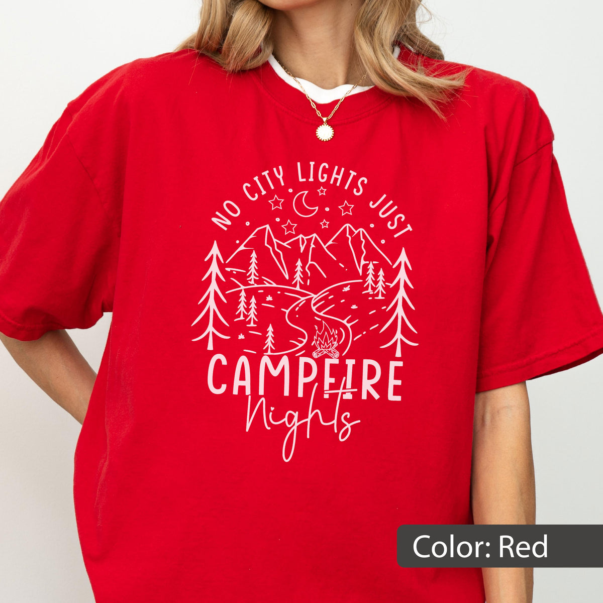May include: A red short-sleeved t-shirt featuring a white graphic print of a mountain landscape with pine trees, a crescent moon, stars, and a campfire. The text reads NO CITY LIGHTS JUST CAMPFIRE Nights in a mix of block and script lettering.