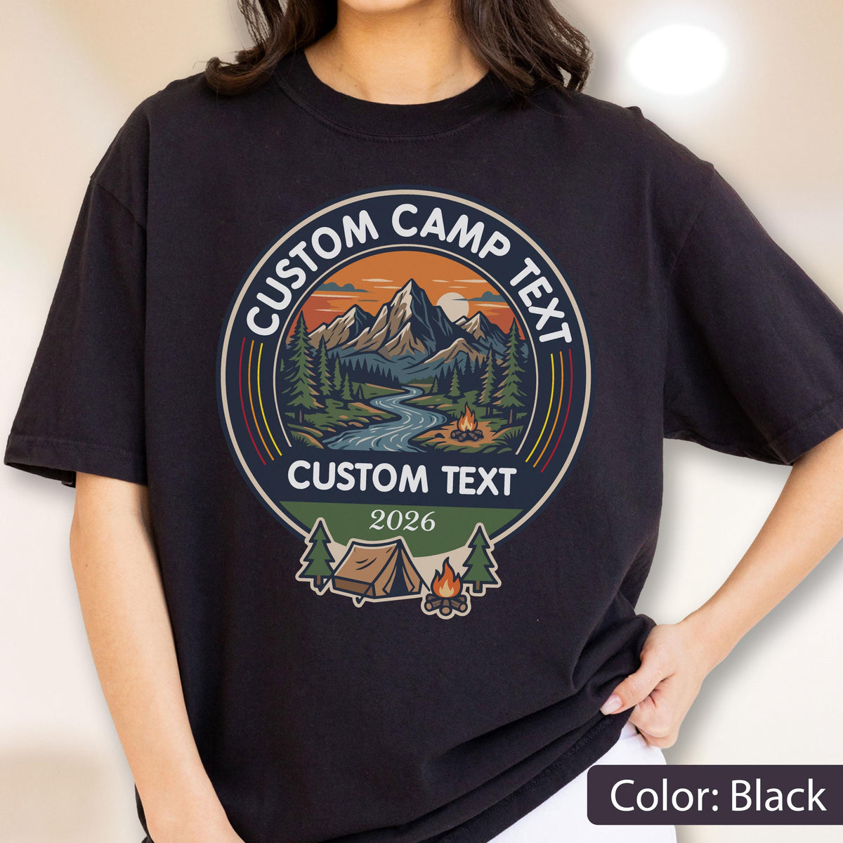 May include: A black t-shirt featuring a circular graphic with a mountain landscape, a river, and a campfire. The text reads CUSTOM CAMP TEXT at the top, CUSTOM TEXT in the middle, and 2026 at the bottom. Below the text is a tent and a small campfire.