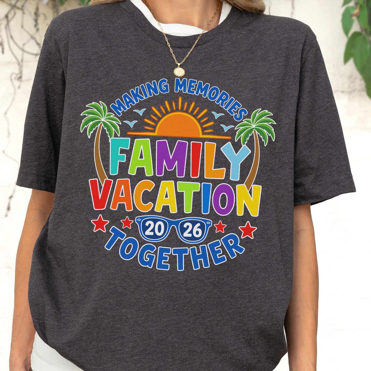 May include: A dark heather gray t-shirt featuring a colorful graphic with the text "MAKING MEMORIES FAMILY VACATION TOGETHER 20 26". The design includes a bright orange sun, green palm trees, blue birds, and blue sunglasses, all arranged in a vibrant, multi-colored layout.