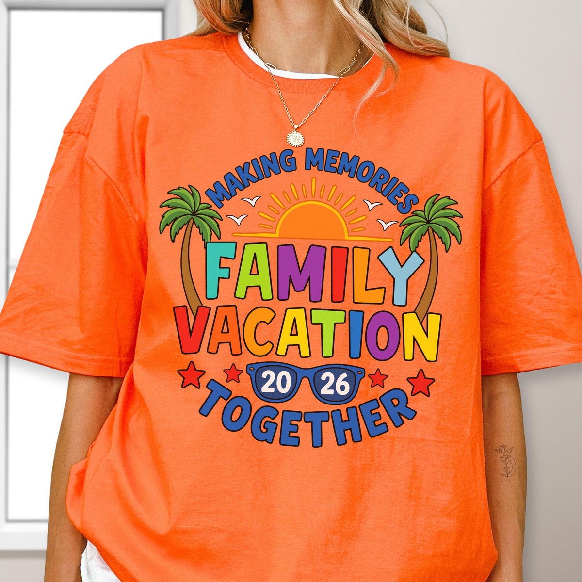 May include: An orange short-sleeve t-shirt featuring a graphic print with the text "MAKING MEMORIES FAMILY VACATION TOGETHER 20 26". The design includes a yellow sun, two green palm trees, and blue sunglasses, all arranged in a colorful layout.