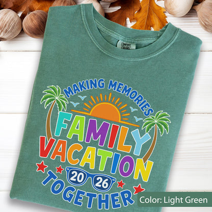 May include: A light green t-shirt featuring a graphic with the text "MAKING MEMORIES FAMILY VACATION TOGETHER 2026". The design includes a bright orange sun, two green palm trees, small blue birds, and a pair of blue sunglasses with the year 2026.