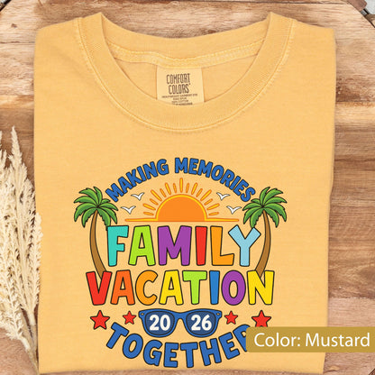 May include: A mustard yellow t-shirt featuring a graphic print with the text "MAKING MEMORIES FAMILY VACATION TOGETHER 20 26". The design includes a bright orange sun, two green palm trees, and blue sunglasses, all rendered in a colorful, bold style.