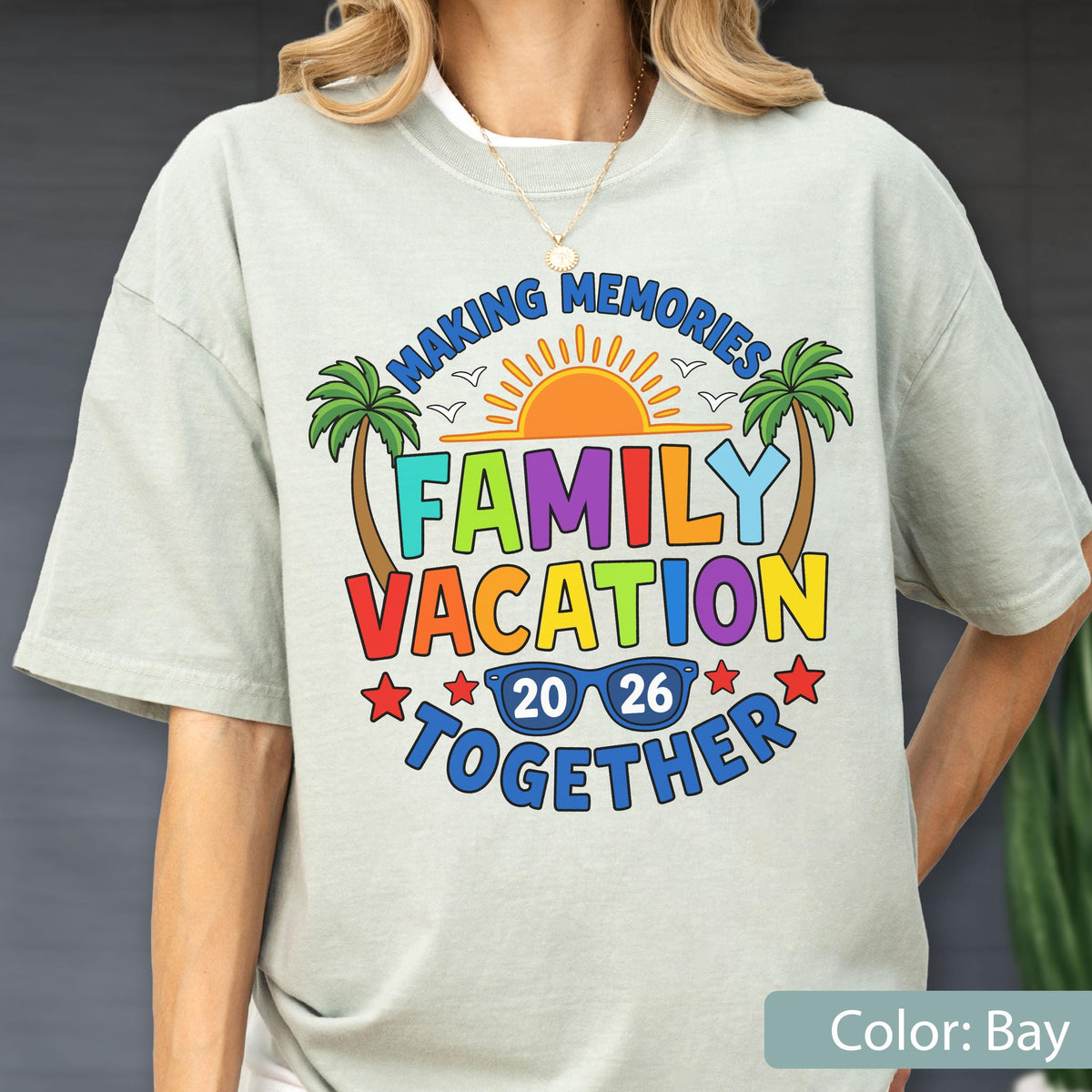 May include: A light gray short-sleeve t-shirt featuring a colorful graphic with the text MAKING MEMORIES FAMILY VACATION TOGETHER 20 26. The design includes a bright orange sun, two palm trees, small birds, and blue sunglasses with the year.