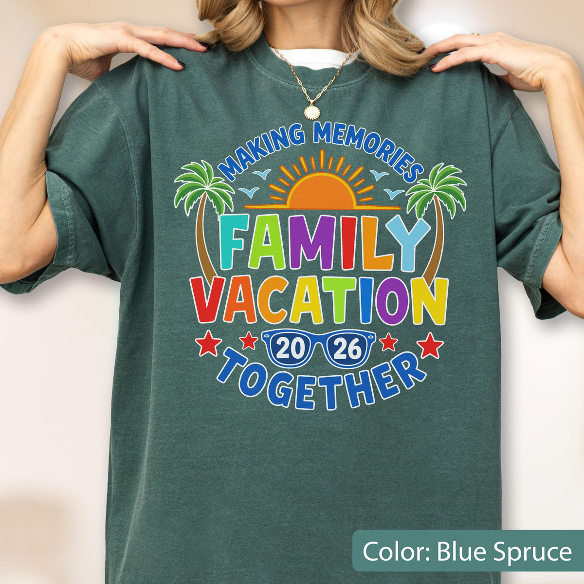 May include: A blue spruce short-sleeve t-shirt featuring a graphic with the text "MAKING MEMORIES FAMILY VACATION TOGETHER 20 26". The design includes a yellow sun, two green palm trees, and blue sunglasses, all set against the dark fabric background.