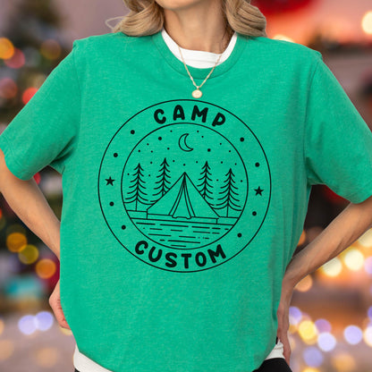May include: A bright green short-sleeved t-shirt featuring a black circular graphic. The design includes a tent, pine trees, a crescent moon, and stars, with the text CAMP CUSTOM printed in a bold, sans-serif font along the circular border.