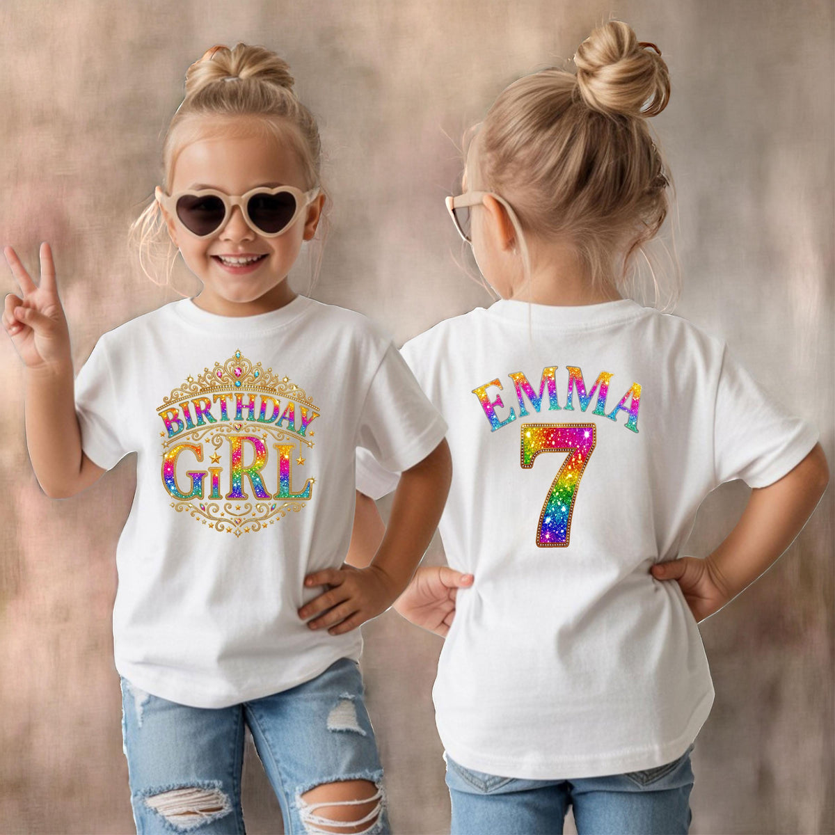 May include: A white t-shirt featuring a gold crown graphic with the rainbow-colored text "BIRTHDAY GIRL" on the front and the name "EMMA" above the number "7" in rainbow-colored glittery text on the back, worn with blue denim jeans.