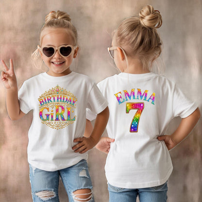 May include: A white t-shirt featuring a gold crown graphic with the rainbow-colored text "BIRTHDAY GIRL" on the front and the name "EMMA" above the number "7" in rainbow-colored glittery text on the back, worn with blue denim jeans.
