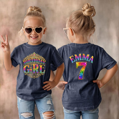 May include: A dark heather navy blue short-sleeve t-shirt. The front features a gold crown graphic with the text "BIRTHDAY GIRL" in a rainbow glitter pattern. The back displays the name "EMMA" and the number "7" in rainbow glitter text.