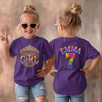 May include: A purple short-sleeved t-shirt featuring a front graphic of a gold crown with the text Birthday Girl in rainbow colors. The back of the shirt displays the name Emma in rainbow letters above a large rainbow-colored number 7.