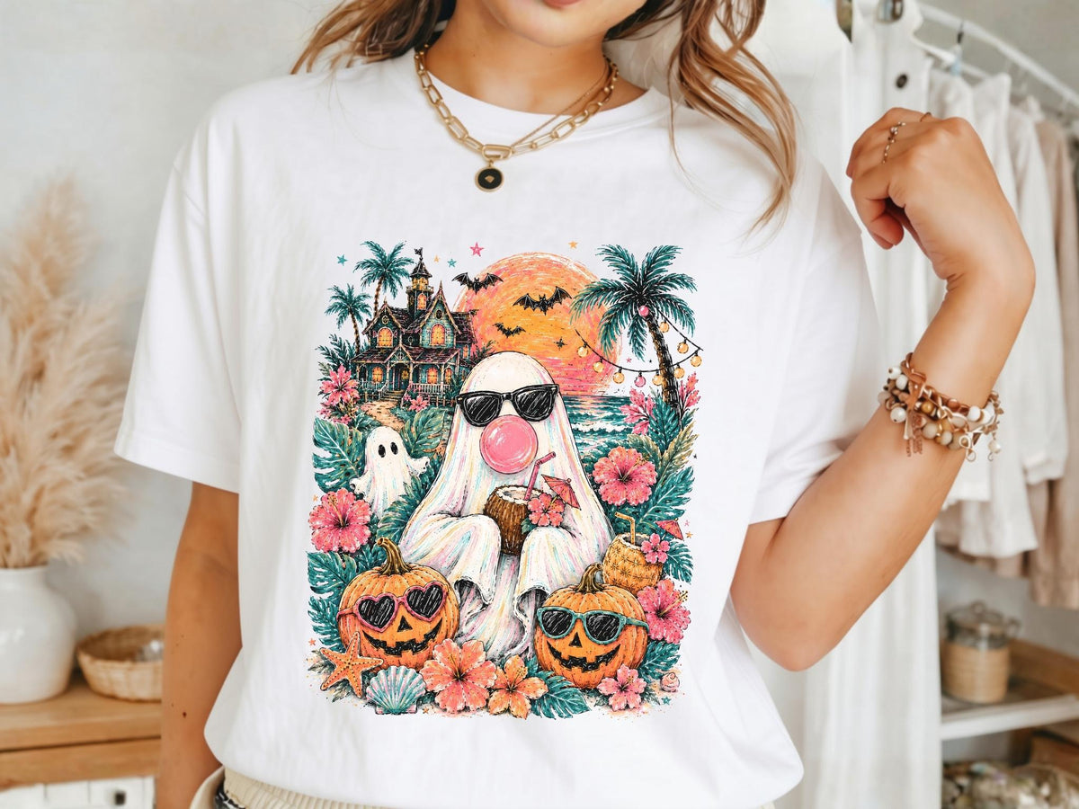 May include: A white t-shirt featuring a colorful graphic of a ghost wearing black sunglasses and blowing a pink bubble. The design includes a tropical beach scene with palm trees, a haunted house, two jack-o'-lanterns, hibiscus flowers, and bats.
