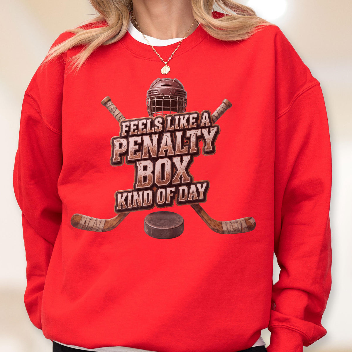 May include: A bright red crewneck sweatshirt featuring a graphic of a hockey helmet, two crossed hockey sticks, and a puck. The text reads, "FEELS LIKE A PENALTY BOX KIND OF DAY," in a distressed brown font centered on the chest of the garment.