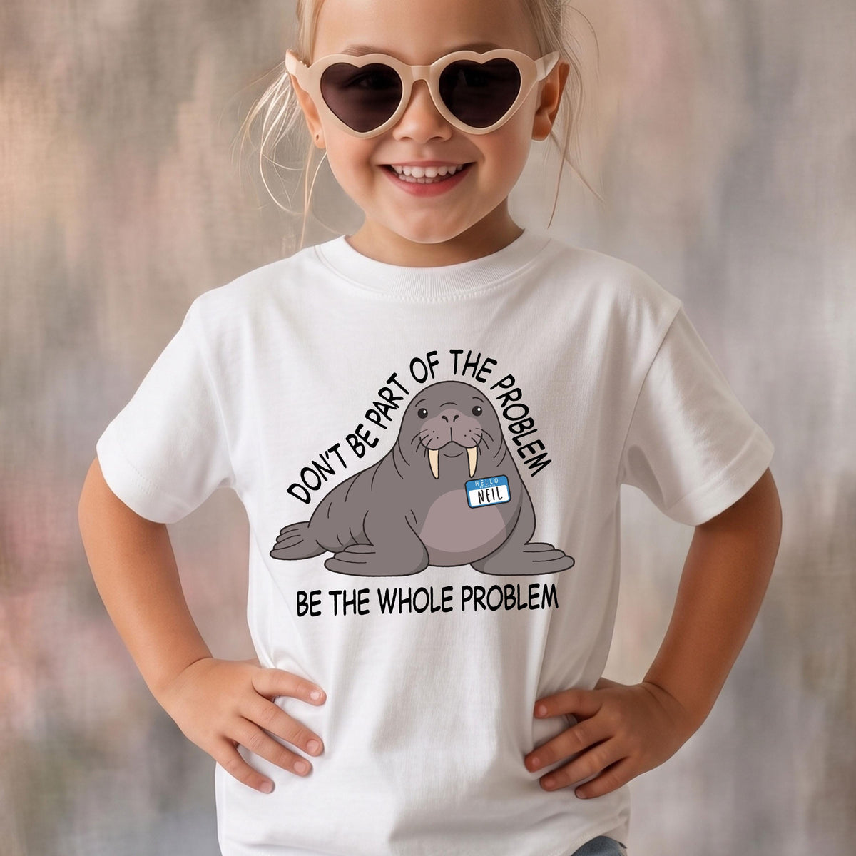 May include: A white t-shirt featuring a graphic of a grey walrus wearing a blue name tag that says NEIL. The text surrounding the walrus reads DON'T BE PART OF THE PROBLEM BE THE WHOLE PROBLEM in black capital letters. The shirt has a crew neckline.