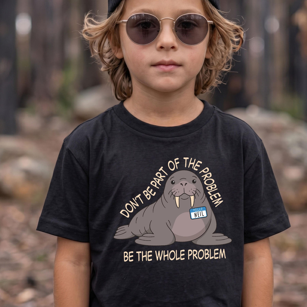 May include: A black t-shirt featuring a graphic of a grey walrus wearing a blue name tag that reads NEIL. The text above the walrus reads DON'T BE PART OF THE PROBLEM and the text below the walrus reads BE THE WHOLE PROBLEM in light tan letters.