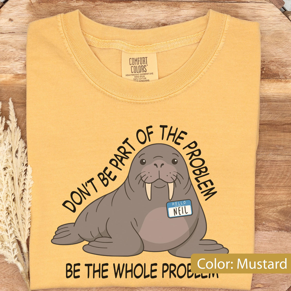May include: A mustard yellow t-shirt featuring a graphic of a brown walrus with tusks wearing a blue name tag that reads HELLO MY NAME IS NEIL. The text DON'T BE PART OF THE PROBLEM BE THE WHOLE PROBLEM is printed in black around the walrus illustration.