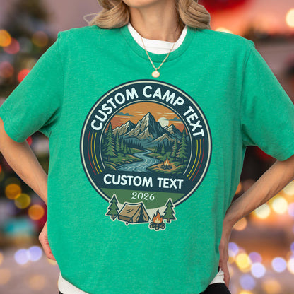May include: A bright green t-shirt featuring a circular graphic with a mountain landscape, a river, and a campfire. The text reads CUSTOM CAMP TEXT at the top, CUSTOM TEXT in the middle, and 2026 at the bottom, with a tent and campfire icon below.