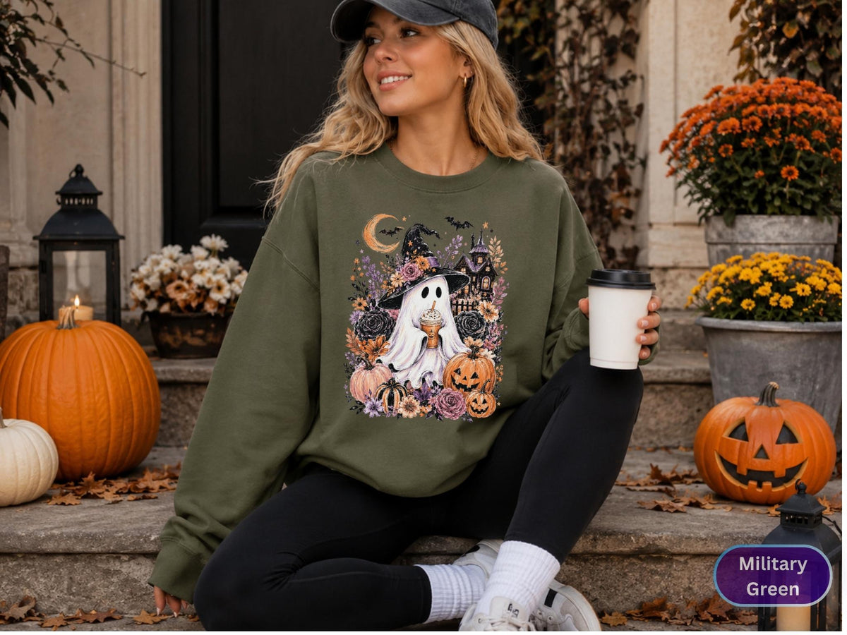 May include: A military green crewneck sweatshirt featuring a graphic print of a ghost wearing a witch hat, surrounded by pumpkins, flowers, a crescent moon, and a haunted house. The sweatshirt has long sleeves and a ribbed collar and cuffs.