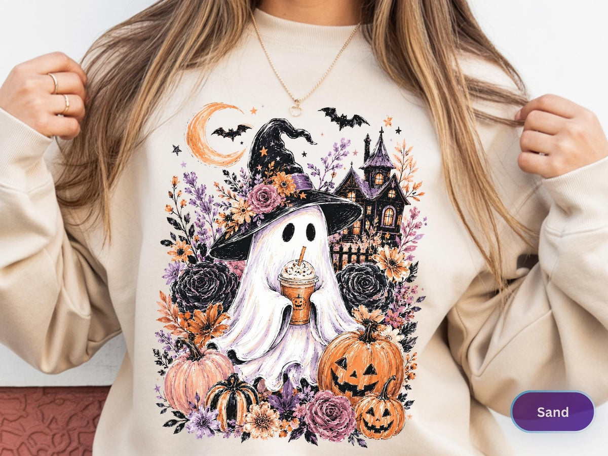 May include: A sand-colored crewneck sweatshirt featuring a graphic print of a ghost wearing a witch hat and holding a coffee cup. The design includes a crescent moon, bats, a haunted house, pumpkins, and various floral elements in orange and purple.
