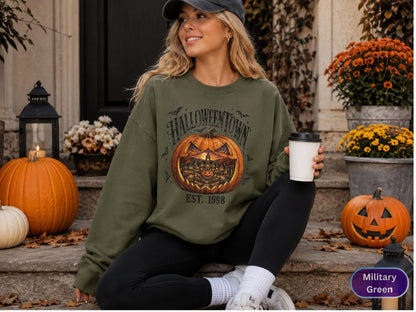 May include: A military green crewneck sweatshirt featuring a large graphic of a carved jack-o'-lantern with a town scene inside. The text reads HALLOWEENTOWN and EST. 1998 in a dark font. The sweatshirt has long sleeves and a ribbed collar.