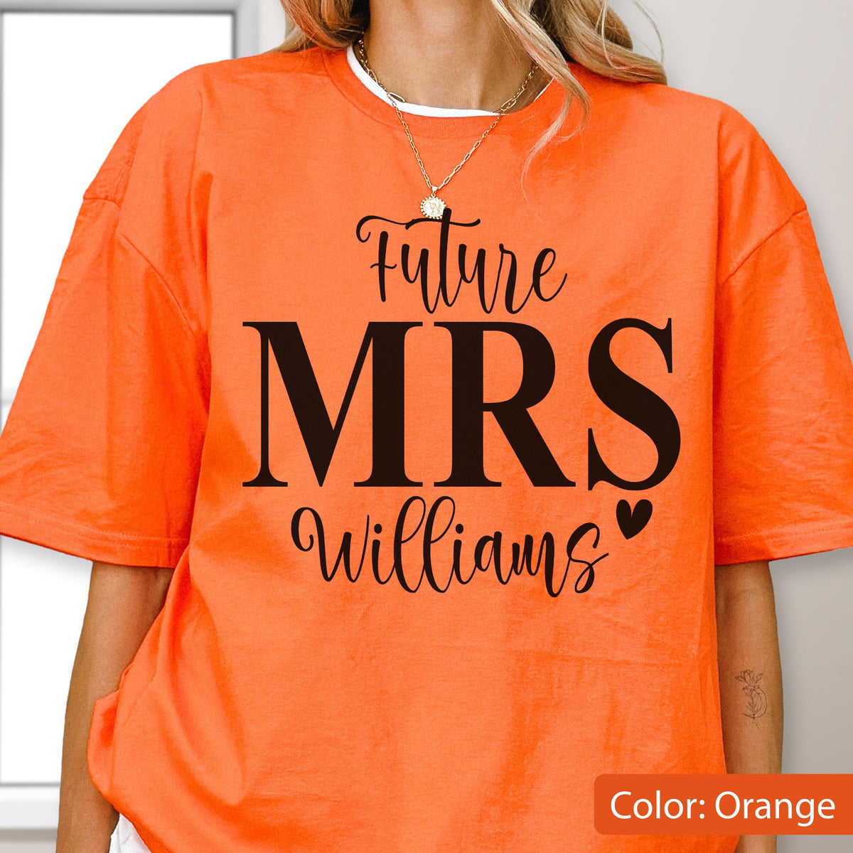 May include: An orange short-sleeved t-shirt featuring black text that reads Future MRS Williams with a small heart icon. The shirt has a crew neckline and a loose fit, showcasing a bold graphic design printed on the front center of the garment.
