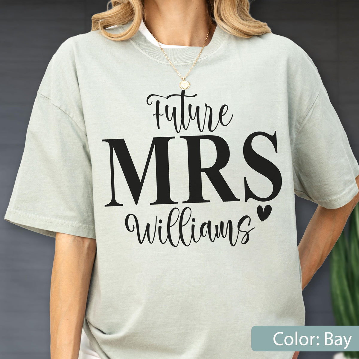 May include: A light sage green short-sleeve t-shirt featuring black text that reads Future MRS Williams with a small heart icon. The shirt has a crew neckline and a relaxed fit, showcasing a simple design printed on the front center of the garment.