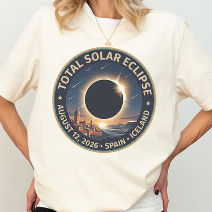 May include: A cream-colored short-sleeve t-shirt featuring a circular graphic of a total solar eclipse over a coastal town. The text reads TOTAL SOLAR ECLIPSE AUGUST 12, 2026 SPAIN ICELAND. The design includes a dark sun, stars, and buildings.