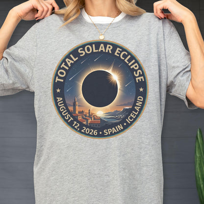May include: A heather gray t-shirt featuring a circular graphic of a total solar eclipse over a coastal town. The text reads Total Solar Eclipse, August 12, 2026, Spain, Iceland. The design includes a dark moon, a glowing sun corona, and stars.