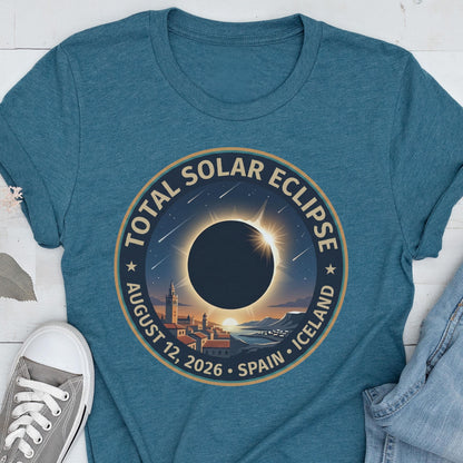 May include: A teal crew neck t-shirt featuring a circular graphic of a total solar eclipse over a town. The text reads TOTAL SOLAR ECLIPSE AUGUST 12, 2026 SPAIN ICELAND. The design includes a dark moon, a bright sun corona, and stars.