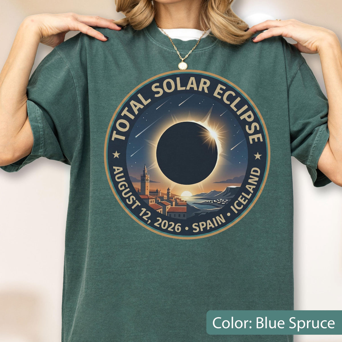 May include: A blue spruce crew neck t-shirt featuring a circular graphic of a total solar eclipse over a coastal town. The text reads TOTAL SOLAR ECLIPSE AUGUST 12, 2026 SPAIN ICELAND. The design includes a dark sun, rays, and stars.