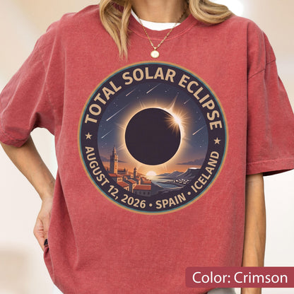 May include: A crimson short-sleeve t-shirt featuring a circular graphic of a total solar eclipse over a coastal town. The text reads TOTAL SOLAR ECLIPSE AUGUST 12, 2026 SPAIN ICELAND. The design includes a dark sun, a bright corona, and stars.