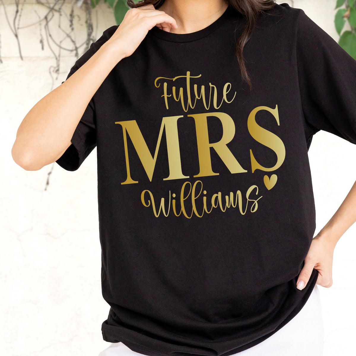 May include: A black short-sleeved t-shirt featuring gold-colored text that reads Future MRS Williams with a small heart icon. The design is centered on the chest, utilizing a combination of a script font for the words Future and Williams.