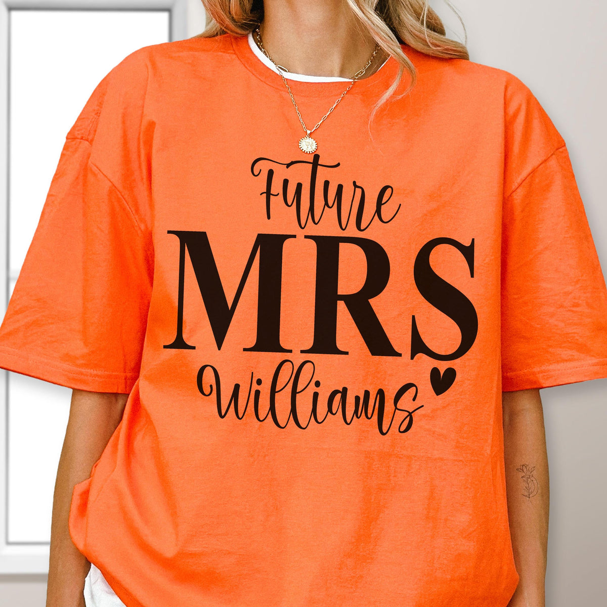 May include: A bright orange short-sleeved t-shirt featuring black text that reads Future MRS Williams with a small heart icon. The shirt has a crew neckline and a loose fit, showcasing a bold graphic design printed on the front center of the garment.