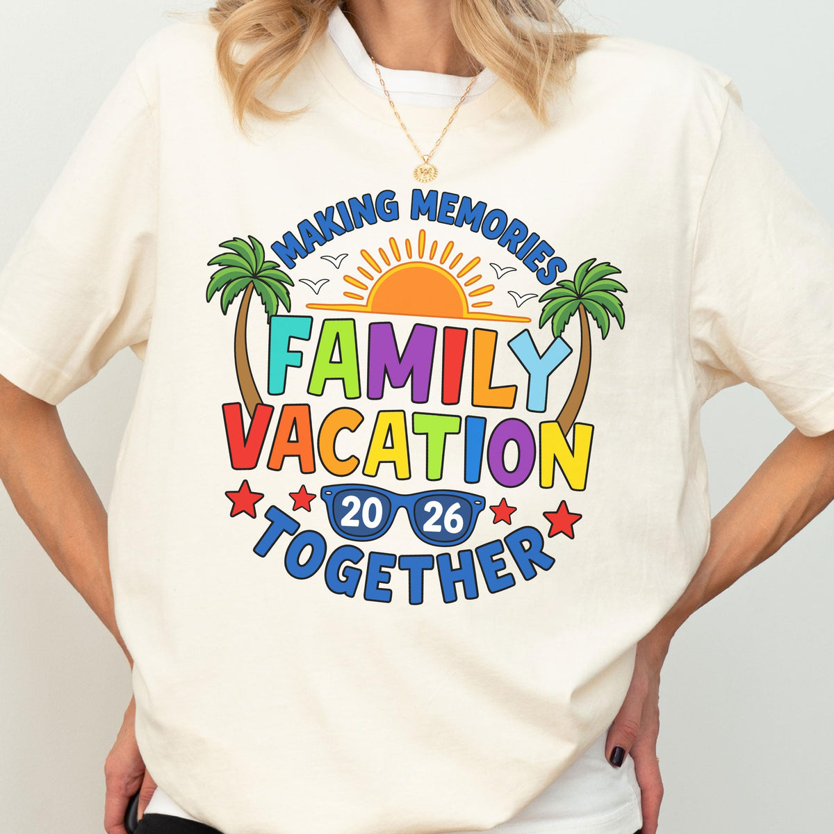 May include: A cream-colored t-shirt featuring a colorful graphic with the text "MAKING MEMORIES FAMILY VACATION TOGETHER 20 26". The design includes a bright orange sun, two green palm trees, blue sunglasses, and red stars, all arranged in a vibrant, multi-colored layout.